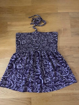 Y2k Lila mönstrad halterneck topp - Säljer en lila topp med vitt paisley-inspirerat mönster och smockad överdel. Toppen har halterneck med knytband och är ärmlös. Perfekt för sommaren och sitter naturligt och mjukt på kroppen. Sitter tight förutom vid volangen 