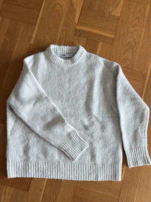 Vit stickad tröja från Zara - Mysig vit stickad tröja från Zara med rund halsringning och ribbade muddar vid ärmslut och nederkant. Tröjan har en enkel och stilren design som passar perfekt till kalla dagar. 
