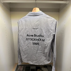 Acne Studios Skjorta ~ Unisex  - 🔷Striped button-up shirt in a cropped fit Clean grey & white vertical stripe pattern 🔷Bold back print from Acne Studios - "Stockholm 1996" 🔷Lightweight cotton fabric - crisp and breathable 🔷Classic collar and button closure Minimal front, statement back 🔷Scandinavian aesthetic - simple, modern, and clean 🔷Easy to style for both casual and elevated looks