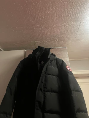 Svart dunjacka från Canada Goose - Säljer en svart dunjacka från Canada Goose med huva och klassisk logotyp på ärmen. Jackan har en rak passform, dragkedja framtill och stora quiltade paneler som ger en riktigt varm känsla. Perfekt för kalla vinterdagar. Priset kan alltid diskuteras vid en snabb affär  🏬 och var inte rädd att komma med frågor om du undrar något😊