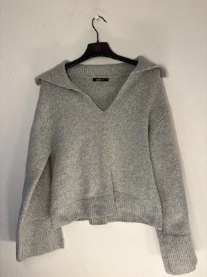 Grå stickad tröja med krage - Mysig grå stickad tröja från Weekday med bred krage och djup v-ringning. Tröjan har långa ärmar med breda ribbade muddar och en avslappnad passform. Perfekt för lager på lager och enkel att styla till olika looks.