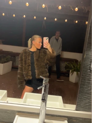 Brun fluffig pälsjacka - Säljer en brun, fluffig pälsjacka med rak passform och rund halsringning. Jackan har långa ärmar och stängs framtill. Perfekt för dig som vill ha en trendig och varm look under vintern. Materialet är fuskpäls som känns mjuk och lyxig. På insidan av jackan så har inre tyger gått upp i sömmen, men annars är den hel och fin och påverkar inte utseende på något sätt. Enbart på insidan de syns🫶🏻