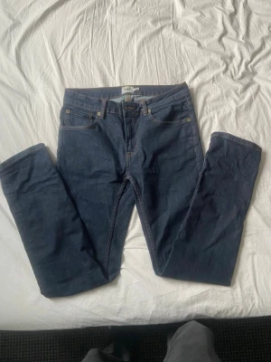 Mörkblå slim fit jeans från lager 157 - Säljer ett par mörkblå slim fit jeans från lager 157. Klassisk femficksdesign med snygga kontrastsömmar och läderpatch bak. Jeansen är tillverkade i denim och har en modern passform som sitter snyggt på benen.