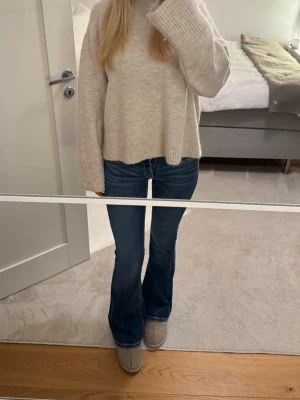 Beige stickad tröja - Mysig beige stickad tröja med oversized passform och långa ärmar. Tröjan har bred ribbstickning vid ärmslut och nederkant samt en hög hals. Perfekt för lager på lager och chill stil. Materialet ser ut att vara mjukt och skönt, troligen bomull eller ullblandning.