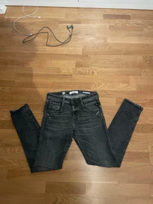 Svarta slim fit jeans från Replay - Säljer ett par svarta slim fit jeans från Replay med klassisk femficksdesign och snygga slitningar. Jeansen har en låg midja och är tillverkade i stretchigt denim som ger en skön passform. Perfekta för dig som gillar en modern och stilren look.
