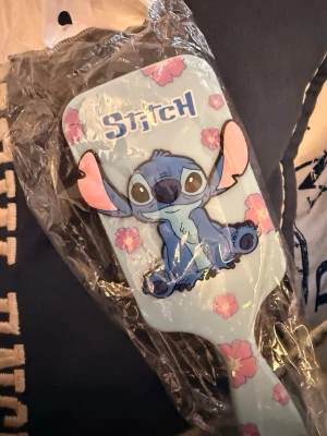 Stitch hårborste med blommor - Söt hårborste i ljusblått med motiv av Stitch från Disney och rosa blommor. Borsten har ett rektangulärt huvud och är tillverkad i plast. Perfekt för dig som gillar roliga accessoarer med karaktärer.