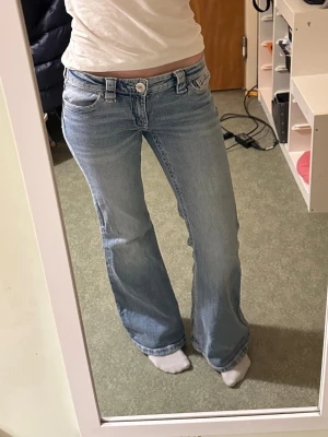 Ljusblå bootcut jeans låg midja - Säljer ett par ljusblå bootcut jeans med klassisk femficksdesign och låg midja. Jeansen har en snygg tvätt och är tillverkade i denim med lite stretch för skön passform samt justerbar resår i midjan. Jag är 168cm lång💕
