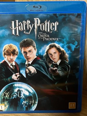 Harry Potter och Fenixorden Blu-ray - Blu-ray-utgåva av filmen 'Harry Potter och Fenixorden' med blå plastfodral. Omslaget har en mörk och magisk design med huvudkaraktärerna i Hogwarts-uniformer och trollstavar. Text på svenska, norska och finska på baksidan. Perfekt för samlare eller filmkväll.