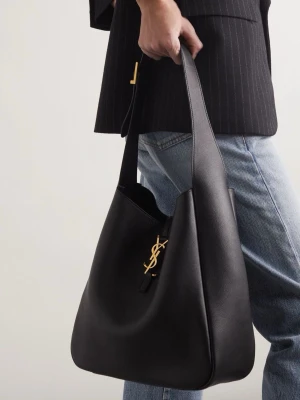 Svart Saint Laurent handväska i läder - Säljer en svart handväska från Saint Laurent i mjukt läder med guldigt YSL-emblem framtill. Väskan har en stilren, rundad form och bred axelrem som gör den enkel att bära. Perfekt för dig som gillar klassisk och lyxig design.