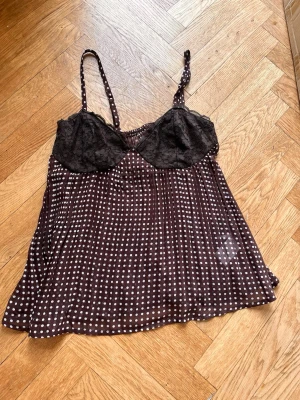 Prickigt blus med blommdetaljer  - Brunt blus med vita prickar och tunna axelband. Överdelen har svarta blommdetaljer och lätt v-ringad form. Luftigt och mjukt material som ger en bekväm känsla, perfekt för somriga dagar. Skriv gärna för mått! 💕