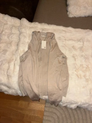 Beige hoodie med dragkedja - Snygg beige hoodie med dragkedja framtill och huva. Tillverkad i mjukt stickat material som känns skönt mot huden. Långa ärmar och ribbade muddar vid ärmslut och nederkant. Perfekt för en avslappnad och stilren look.