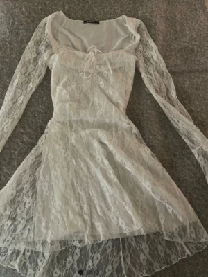 Vit spetsklänning från Gina Tricot - vit klänning från Gina Tricot i spets med långa ärmar och söt knytning vid urringningen.                              Klänningen har en lätt utsvängd kjol och transparenta fina spetsdetaljer! 💞💞