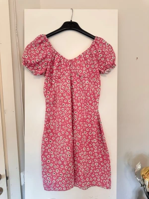 Rosa blommig kortklänning - Söt rosa kortklänning med vita blommor, Klänningen har en lätt uringning framtill   och är tillverkad i ett mjukt tyg som passar perfekt till sommaren, och är superfin till sneakers eller sandaler, klänningen har egentligen varit en midi klänning men som jag varit hos en skräddare och sytt ner till en mini, står storlek L men den är som en M 
