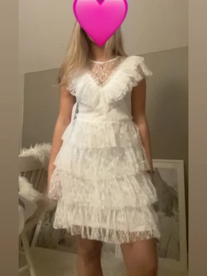 Vit spetsklänning med volanger - Nu säljer jag min fina fina studentklänning!Supersöt vit kortklänning i spets med flera lager volanger och v-ringad. Perfekt för sommarens alla tillfällen och studentfirande. Använd en gång. Så som ny!! Köpt för 900kr🩷