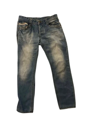 Blå raka jeans från Diesel - Snygga blå jeans från Diesel med raka ben och slitna detaljer på fram- och baksida. Klassisk femficksmodell med knappgylf och ljusa tvättade partier för en cool look. Tillverkade i mjuk denim som ger en avslappnad känsla.