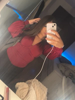 Nelly - Snygg vinröd omlottblus med djup v-ringning och långa puffärmar. Blusen har en figurnära passform och markerad midja. Jag har använt denna vid ett tillfälle vilket var under nyår. Den har en jätte bra passform som ni kan se på bilden och är hur snygg som helst. Men tyvärr så har jag ingen mer användning av den därför säljer jag den.