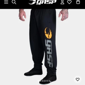 GASP träningsbyxor med tryck - Säljer två par träningsbyxor från GASP, ett par svarta med stort GASP-tryck och orange logga på benet, och ett par grå med texten 'NO COMPROMISES NO EXCUSES' längs benet samt logga. Båda har dragsko i midjan och är i loose fit, perfekta för gymmet. Båda är i strl S och vanlig längd (alltså inte tall). 