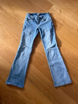 Ljusblå bootcut jeans med fjärilar - Säljer ett par ljusblå bootcut jeans med snygga broderade fjärilar på bakfickorna. Jeansen har klassisk femficksmodell, normal midja och dragkedja med knapp. Perfekta för dig som gillar en retro och unik stil!