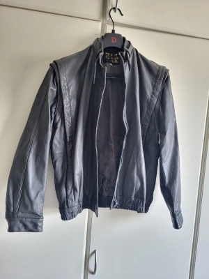 Svart klassisk skinnjacka herr - Snygg svart skinnjacka med rak passform och ståkrage. Jackan har dragkedja framtill, diskreta sömdetaljer och elastisk midja. Perfekt för dig som vill ha en tidlös och stilren look. Passar till jeans och t-shirt för en avslappnad vibe.