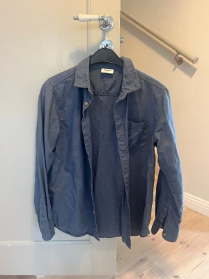 Mörkblå skjorta från Kappahl - Snygg mörkblå skjorta från Kappahl med klassisk krage och bröstficka. Skjortan har långa ärmar och knappar framtill. 