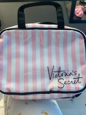 Rosa och vitrandig necessär från Victoria’s Secret  - Söt necessär med rosa och vita ränder på utsidan och svart handtag. Insidan har svart tyg med små rosa prickar och flera genomskinliga fack för smink eller småprylar. Perfekt för att organisera dina grejer när du är på språng. Finns ej att köpa längre 