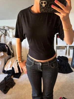 Svart croppad topp från 157 - Säljer en svart croppad topp från 157 i mjukt material. T-shirten har rund halsringning och korta ärmar, perfekt för en chill och enkel stil. Passformen är normal och toppen är enkel att matcha med olika outfits.