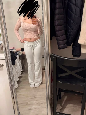 Ljusrosa croppad topp med blommor - Söt croppad topp i ljusrosa med små blommor som mönster. Toppen har långa ärmar, en lätt v-ringad urringning och är figurnära i modellen. Perfekt för dig som gillar gulliga detaljer och en feminin stil.