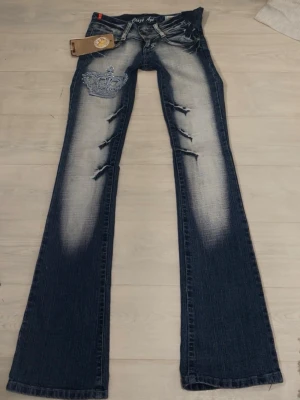 Blå bootcut jeans Crazy Age krona - Säljer ett par blå jeans från Crazy Age. Mått Innerbenet:84cm ytterben:100cm Midjemått: 35,5cm Grenmåttet: 16cm Storlek 32/22. Extremt eftertraktade Crazy Age–jeans med unika detaljer. Extremt lågmidjade, tajta i låren, bootcut och långa – äkta 2000–tals passform. Väldigt få par finns kvar. Original Crazy Age–lapp kvar. Jag har sytt ut midjan lite (se sista bilden), men man kan sy ihop dem igen. Kom privat för mer bilder elr frågor!💘 
