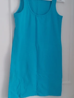 Turkos ärmlös bomullsklänning - En enkel och snygg turkos klänning i bomull med ärmlös design och rund halsringning. Perfekt för varma dagar och lätt att styla med accessoarer. Klänningen har en rak passform och slutar ovanför knäna.