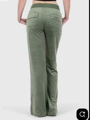 Juicy Couture gröna velourbyxor - Gröna mjukisbyxor i mjuk velour från Juicy Couture. Byxorna har raka ben, bred resår i midjan med dragsko, fickor fram och bak samt en liten logga på ena benet. Perfekt för en chill och trendig vibe.