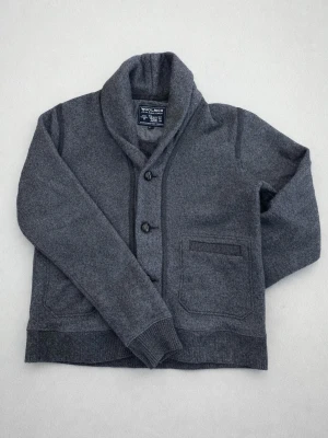 Grå kofta från Woolrich med sjalkrage - Mysig grå stickad cardigan från Woolrich med  Perfekt för lager på lager och en chill look. Materialet är ullblandning som håller dig varm, perfekt nu på våran och kyligare sommarkvällar. Den är liiiiite för liten för mig som är cirka 180. Tveka inte att höra av dig vid frågor🤩