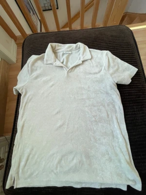 Vit pikétröja från Kappahl - Klassisk beige pikétröja från Kappahl i mjukt frottéliknande material. Tröjan har korta ärmar, krage och knappfri öppning framtill. Perfekt för en avslappnad och stilren look.