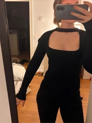 Svart långärmad topp med cut out - Trendig svart långärmad topp med snygg cut out-detalj över bröstet och hög hals. Figurnära passform som ger en cool och stilren look. Perfekt att styla med jeans eller kjol för en edgy vibe.