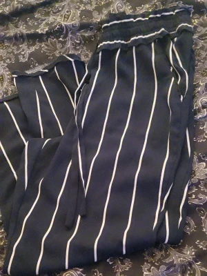 Blåa randiga byxor med dragsko från Zara  - Säljer ett par blåa byxor med vita vertikala ränder och elastisk midja med dragsko. Byxorna har avslappnad passform och är tillverkade i ett mjukt, tunt material som känns skönt mot huden. Perfekta för en chill och stilren look och passar perfekt till våren och sommaren 