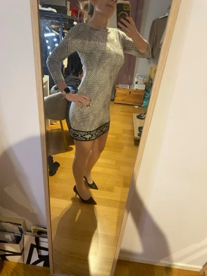 Mönstrad kort klänning med långa ärmar - Mikael Kors klänning. Snygg kort klänning i svartvitt mönster med lång ärm och rund halsringning. Klänningen har en dekorativ svart bård längst ner och figurnära passform. Perfekt för dig som gillar stilrena och trendiga plagg. Passar även M.