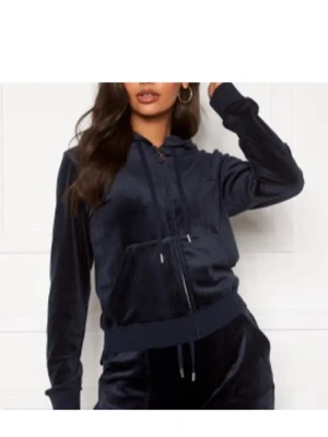 Mörkblå velour hoodie Juicy Couture - Snygg mörkblå hoodie i mjuk velour från Juicy Couture. Dragkedja framtill, fickor och justerbar huva med snören. Ikonisk JC-logga broderad på bröstet och på snörena. Passar M och L 