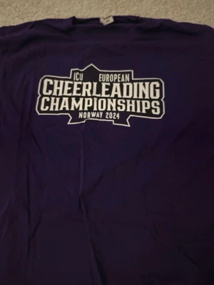 Lila staff t-shirt ICU Cheerleading - Unik lila t-shirt från ICU European Cheerleading Championships Norway 2024. Tryck fram med eventets logga och texten 'STAFF' på ryggen omgiven av vita stjärnor. Perfekt för dig som vill ha ett minne från tävlingen eller gillar cheerleading-vibe.