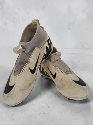 Nike Air Zoom vita fotbollsskor - Säljer ett par vita Nike Air Zoom fotbollsskor med svarta detaljer och stora swoosh-loggor. Skorna har en strumpliknande passform utan snörning och elastiska band över vristen. Yttermaterialet är syntetiskt och sulan har dobbar för bra grepp på planen.