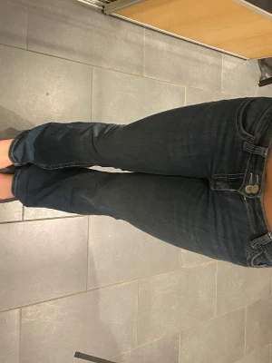 Mörkblå bootcut jeans med broderi - Använd en gång och är i helt nytt skick! Snygga mörkblå bootcut jeans med dubbla knappar och broderade bakfickor. Jeansen har klassisk femficksmodell och kontrastsömmar. Perfekta för dig som gillar en avslappnad men trendig look.