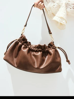 SÖKER!!! jätte fin väska från H&M skriv till mig tack🤩  - Trendig brun handväska med scrunchie-detaljer och justerbar axelrem. Väskan har en mjuk, rynkad design och är tillverkad i skinnimitation. Perfekt för dig som gillar en avslappnad men stilren look.