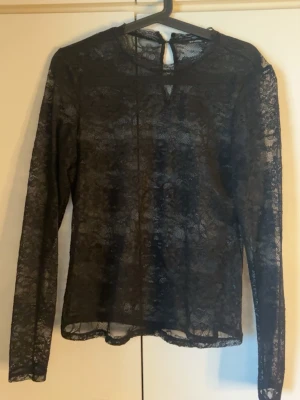 Svart spetsblus - Säljer en helt ny svart långärmad spetsblus från Studio/ Vero moda. Blusen har rund halsringning, transparent spetsmaterial och knappdetalj i nacken. Perfekt för dig som gillar en elegant och trendig look. Aldrig använd❤️