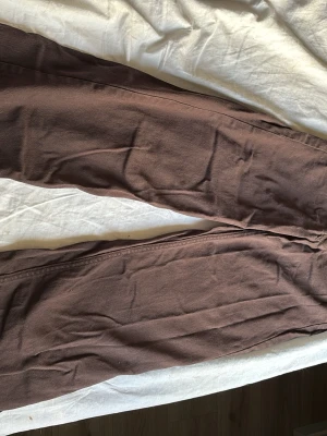 Bruna raka jeans med hög midja - Säljer ett par bruna jeans med rak passform och hög midja. Klassisk femficksmodell med knapp och dragkedja framtill. Jeansen har bälteshällor och är gjorda i ett kraftigare bomullstyg. Perfekta för en avslappnad och trendig look.