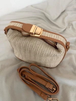 Beige stickad handväska med läderdetaljer - Trendig beige handväska med stickad struktur och snygga ljusbruna läderdetaljer. Väskan har guldfärgat spänne, dragkedja och avtagbar axelrem i matchande läder. Perfekt accessoar för en avslappnad men stilren look.