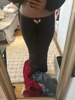 Svarta mjukisbyxor med tryck - Säljer ett par bruna mjukisbyxor med rosa  detaljer '2002' på baksidan och rosa snören  framtill i midjan. Byxorna har utsvängda ben och är perfekta för en chill och avslappnad stil. Materialet känns mjukt och bekvämt, perfekt för att hänga hemma eller dra till kompisar.dom är snygga men även jätte sköna på. Jag säljer dessa för att dom är förkorta i benen för mig och har använt dom typ 2 eller 3 gånger 