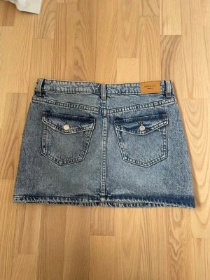 Blå jeanskjol med fickor - Snygg blå jeanskjol i klassisk modell. Kjolen har en kort längd och är gjord i slitstarkt denimtyg. Perfekt att matcha med en t-shirt eller hoodie för en avslappnad look.