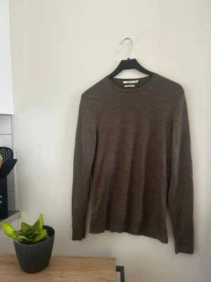 Brun merinoulltröja från Selected Homme - Säljer en tunn, brun stickad tröja från Jack & Jones  i superfin merinoull. Tröjan har rund halsringning och långa ärmar, perfekt för lager på lager och en clean look. Enkel och stilren design som passar till det mesta. Tröjan har en lagning på höger arm!