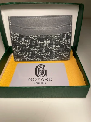 Grå kortfodral från Go4yard - Snyggt grått kortfodral från Go4yard med klassiskt mönster och vit logga framtill. Tillverkat i canvas och läder, perfekt för kort och ID. Kommer i original grön ask med gul putsduk och Go4yard-kort.