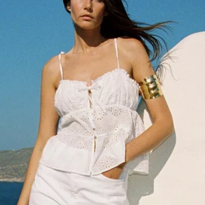 Vit broderad linnetopp med knyt - Söt vit linnetopp med broderade detaljer och tunna axelband som knyts upptill. Toppen har en liten rosett framtill och en luftig, volangig nederdel. Perfekt för varma dagar och ger en romantisk vibe. (Prislapp kvar!!)