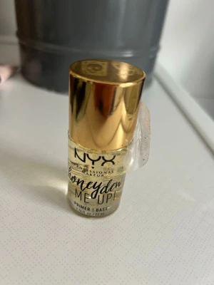 NYX Honey Dew Me Up Primer - NYX Honey Dew Me Up Primer är en genomskinlig primer med guldfärgade detaljer och en lyxig guldig kork. Formulan är gelbaserad och kommer i en liten glasflaska. Perfekt för att skapa en fräsch och återfuktad bas innan sminket.