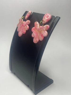 Rosa swirl örhängen - Unika handgjorda örhängen i resin med rosa och vita swirlmönster samt inslag av guldglitter. Örhängena har en lekfull, blomliknande form och sitter i guldfärgade ringar. Perfekta för dig som vill sticka ut med färg och kreativ design.